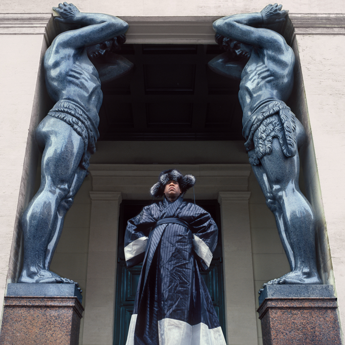 Andre Leon Talley, Vogue magazine's editor at large on his visit to Russia. Flanked by two giant Atlases, ALT stands at the side entrance to Hermitage Museum, St. Petersburg. Andre Leon Talley's outfit consists of kimono by Christian Dior Haute Couture and fur hat by Prada.